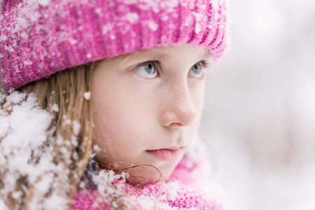A closeup of a child in pink hat and snow on hair and serious look.の写真素材