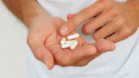 Close-up of a man's hand holding medicine capsules and about to take them