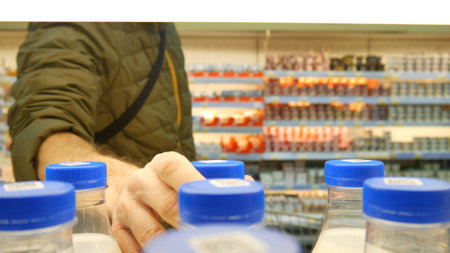 Close-up of many milk bottles with blue caps on a supermarket shelf and a man takes oneの写真素材