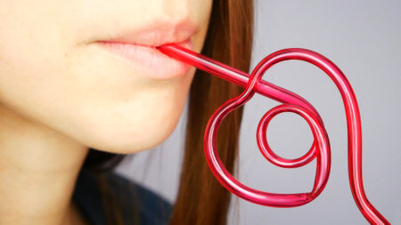 A very beautiful girl drinks from a pink heart-shaped straw close-up