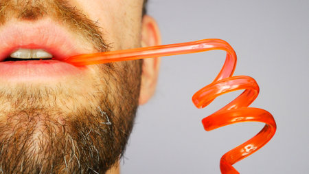 Close-up of a bearded man's mouth drinking from a twisted strawの写真素材