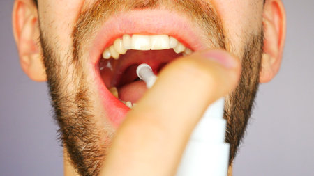 A young man sprinkles spray into the mouth close-up