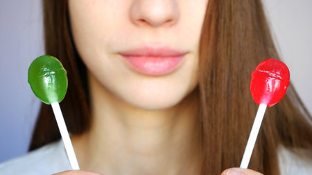 Close-up of red and green lollipops in the hands of a young woman against them