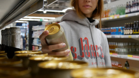 Close-up of a cute girls hand taking a golden can of beer in a supermarketの写真素材
