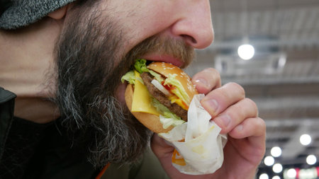 A bearded man biting a beautiful tasty hamburger in his hand close-upの写真素材