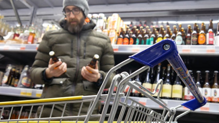 Close-up of a shopping trolley in alcohol department and a male buyer choosing the bottles of beer...