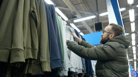 A male buyer choosing a gray hoodie in a clothing store