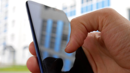 Close-up of a smartphone in the hand of a man typing a message outdoors