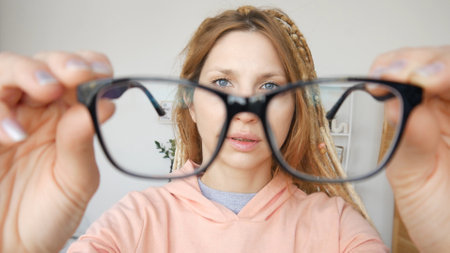 A cute girl looking through black-framed glasses in her hands