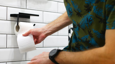 A man unrolling toilet paper while sitting on the toilet close-upの写真素材