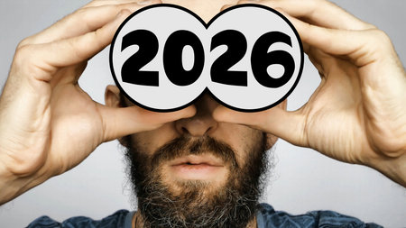 Close-up of a bearded man holding depicted binoculars to his eyes with the big number 2026