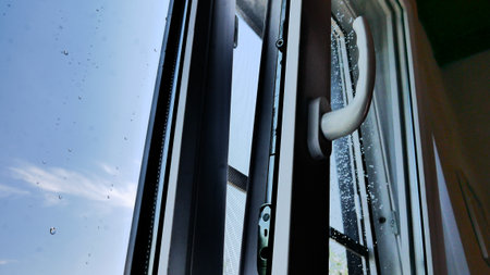 Close-up of an open window sash with rain drops on the glass