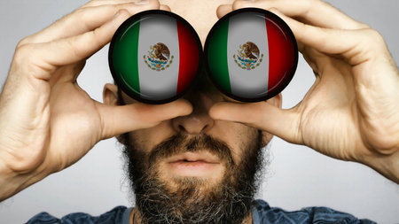 The Mexican flag is reflected in the lenses of binoculars through which a bearded man looks