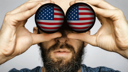 The USA flag is reflected in the lenses of binoculars through which a bearded man looks