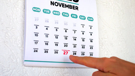 A male hand pointing finger to the date of Thanksgiving 2025 highlighted on a wall calendarの写真素材