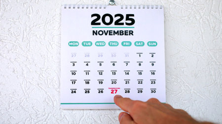 A male hand pointing finger to the date of Thanksgiving 2025 highlighted on a wall calendarの写真素材