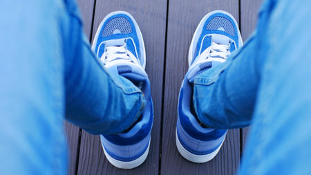 A view from the eyes of a sitting man's legs in blue jeans and sneakersの写真素材