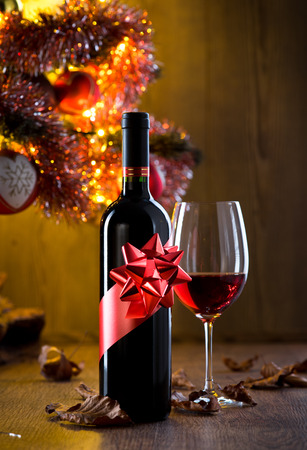 Wine bottle gift and wine glass filled with red wine, christmas tree and dry leaves on background.の写真素材