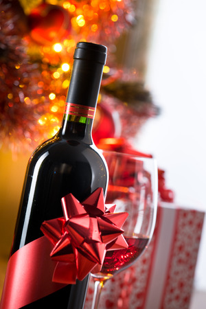 Wine bottle with ribbon and filled wineglass, christmas tree and gift boxes on background.の写真素材