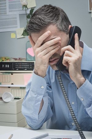 Stressed employee on the phone touching his forehead.の写真素材