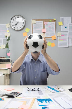 Businessman in his office holding a soccer ball in front of his face.の写真素材