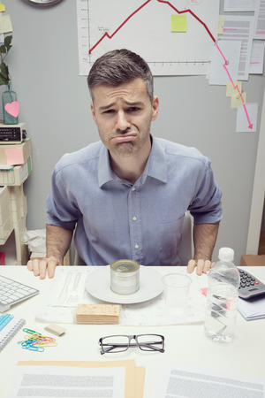 Sad businessman having lunch with canned food and negative business chart on background.の写真素材