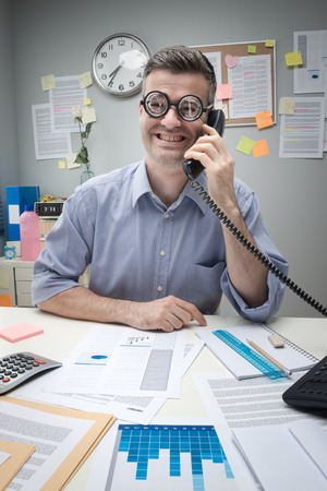 Nerd office worker on the phone sitting at desk and smiling.の写真素材