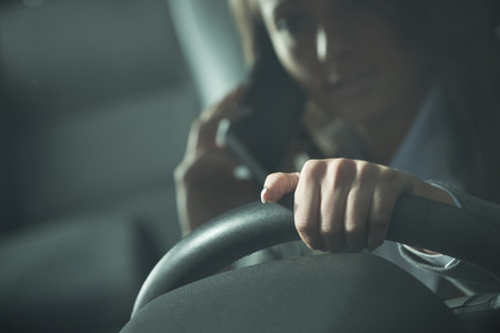 Young woman calling on the phone while driving late at night.の写真素材