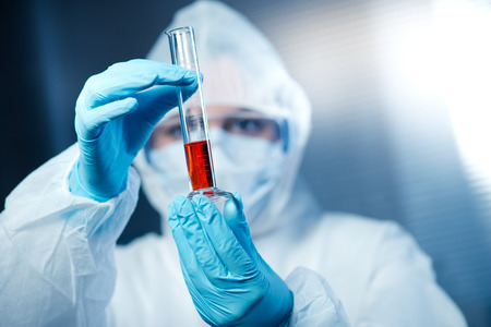 Scientist wearing protective suit and examining a test tube.