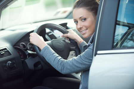 Smiling attractive young woman driving her car and looking at camera.