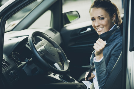 Young attractive woman sitting on car seat and fastening seat belt, car safety concept.