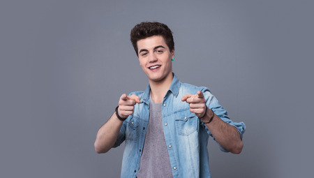 Young confident teenager guy smiling and pointing at camera