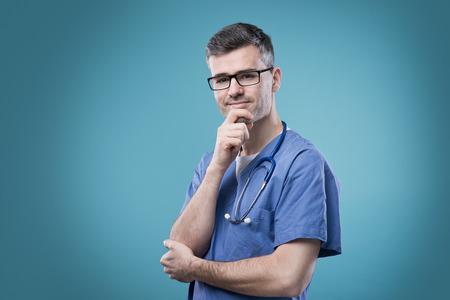 Smiling confident doctor thinking with hand on chinの写真素材