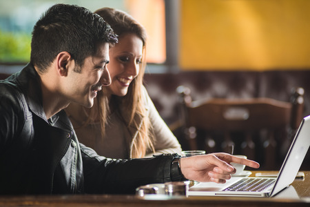 Cheerful couple at the cafe with a laptop, he is pointing at the screenの写真素材