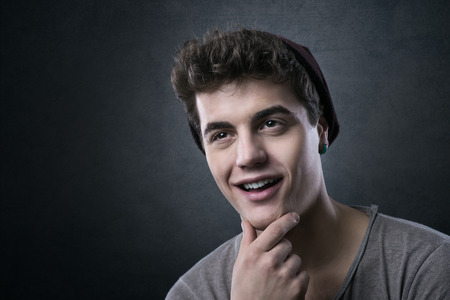 Smiling handsome young man posing with hand on chin on dark backgroundの写真素材