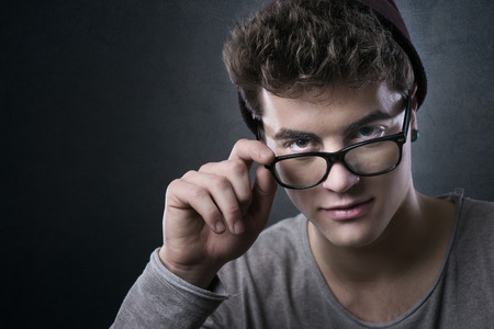 Cool young man adjusting his stylish glasses with flirty expressionの写真素材
