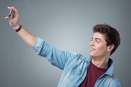 Smiling teenager taking selfies with his smart phoneの写真素材