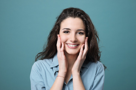 Cheerful young woman smiling and touching her cheeks, freshness and beauty concept