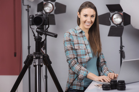 Female photographer working in her professional photo studio with a laptop, camera and lighting...