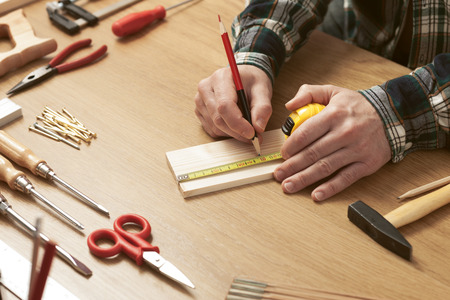Man working on a DIY project and measuring a wooden plank with work tools all around, hands close upの写真素材
