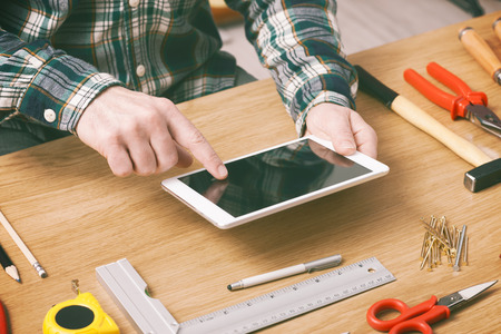 Man working on a DIY project at home with a digital tablet, carpentry and construction tools on a work table, hands close upの写真素材