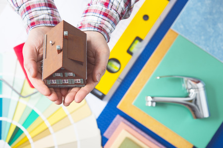 Home insurance, repair and decorating service concept with cupped hands holding a model house and faucet, color swatches and work tools の写真素材