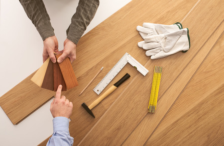 Carpenter showing some wooden baseboard swatches to a customer and choosing a color, flooring installation and work tools on backgroundの写真素材