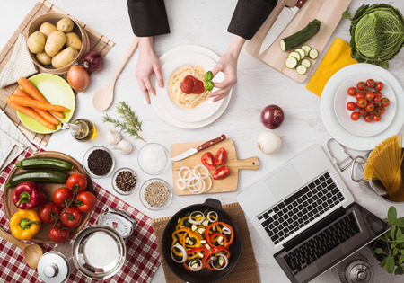 Professional chef's hands cooking pasta on a wooden worktop with vegetables, food ingredients and utensils, top view