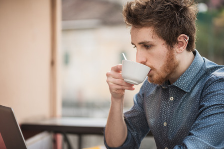  guy having a cappuccino at the bar, he is staring at a laptop screenの写真素材