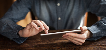 Young man using a digital touch screen tablet on a wooden table, hands close up