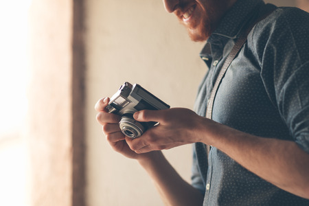  young man holding a vintage camera and checking settingsの写真素材