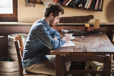 Young  guy having a coffee break in a bar and sketching on his notebookの写真素材