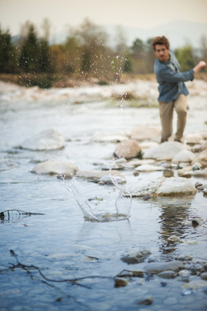 Young man throwing stones in the river and water splash, nature and freedom conceptの写真素材