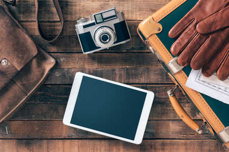 Vintage hipster traveler packing ready to leave with camera and digital touch screen tablet, top view